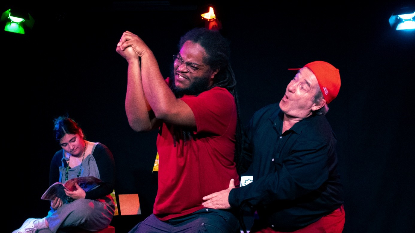 2 comédiens au premier plan tandis qu'une comédienne est assise à l'arriere plan