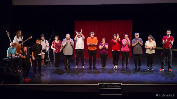 Une quinzaine de comédiens et musiciens applaudissent debout sur scène